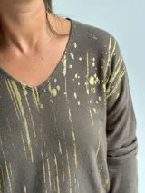 Sweater de punto color verde seco con estampado de salpicaduras en color dorado, cuello en V y mangas largas.