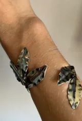 Brazalete rígido abierto de metal plateado con diseño de hojas texturizadas en los extremos.