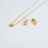 Set de joyería compuesto por un collar con dije de punto de luz y un par de aros tipo caravanas a juego. Ambas piezas presentan circonias engarzadas en bases circulares con baño de oro.