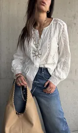 Camisa blanca de manga larga con detalles de encaje y diseño abotonado en la parte delantera.