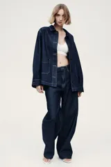 Campera camisera en denim rígido color azul, con cuello camisero, cierre frontal de botones, bolsillos de parche delanteros y bajo redondeado.