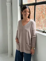 Sweater de punto color visón con escote en V, mangas largas con puños acanalados, corte holgado y dos bolsillos frontales tipo parche.