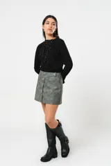 Minifalda gris con textura símil cuero, corte irregular con sobrefalda y cierre frontal con broches metálicos.