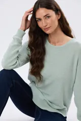 Buzo tejido liso de manga larga con cuello redondo, confeccionado en algodón de tejido grueso. Presenta bordes acanalados en el cuello, los puños y la cintura, con un pequeño detalle de placa metálica en el lateral inferior.