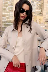 Camisa de cuero ovino en color beige, con cuello camisero, cierre frontal mediante broches metálicos a presión y mangas largas con puños.