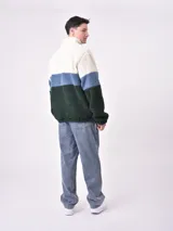 Buzo de tejido polar texturizado, color azul petróleo, con cuello alto y cierre parcial frontal. Presenta un diseño de bloques de color horizontal: blanco crema en la parte superior, gris claro en el medio y azul petróleo en la parte inferior y mangas.