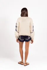 Sweater de punto 100% lana merino en color marfil, de calce holgado y cuello redondo, con detalles bordados en azul marino y flecos decorativos en el bajo y las mangas.