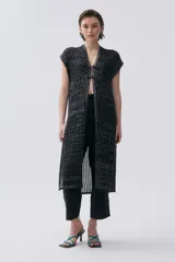 Kimono tejido de punto en color crudo con sutil brillo de lurex. Presenta un diseño sin mangas, corte largo y cierre frontal mediante dos lazos finos. El tejido tiene una textura acanalada vertical.