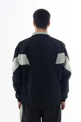 Campera negra de nylon con recortes en forma de V en color gris en las mangas. Tiene cuello mao, cierre frontal, puños y cintura elásticos, bolsillos laterales y logo estampado en el pecho y en la manga izquierda.