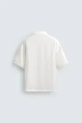 Camisa de corte relajado confeccionada en tejido fluido con textura acanalada. Presenta cuello solapa, manga corta y cierre frontal con botones.