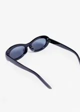 Lentes de sol unisex con armazón ovalado color rosa claro y lentes oscuros.