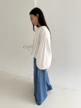 Blusa blanca con cuello mao y cierre frontal de botones de nácar. Presenta mangas largas abullonadas con puños elásticos y detalle de tablas verticales en el frente.