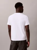 Remera blanca de algodón con cuello redondo y manga corta, presentando un estampado gráfico apilado en negro con el texto "CALVIN KLEIN JEANS".