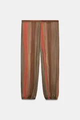 Pantalón semitransparente de tiro medio, corte bombacho con cintura y puños elásticos, con diseño de rayas verticales en tonos marrones y rojizos.