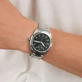 Reloj analógico Armani Exchange modelo Giacomo con caja y malla de acero inoxidable plateado. Presenta una esfera negra con índices luminiscentes en tono verde lima, manecillas plateadas y ventana de fecha a las seis.