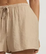 Short de playa color beige, confeccionado en viscosa y poliamida, con diseño holgado, bolsillos laterales, cintura elástica con cordón de ajuste tipo lazo y detalle de botones frontales.