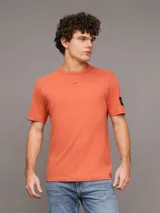 Remera color naranja de corte clásico y manga corta. Tiene cuello redondo y una insignia con el monograma de Calvin Klein en la manga.