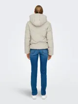 Campera acolchada color beige claro, repelente al agua, con capucha fija y cierre frontal de cremallera. Presenta un diseño acolchado con costuras en forma de 'V' invertida en el torso y puños internos en las mangas.