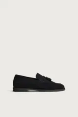 Mocasín de vestir negro confeccionado en piel con acabado serraje, con detalle de borlas en el empeine y ligero tacón.