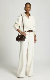 Pantalón sastrero de pierna ancha y tiro medio color marfil, confeccionado en algodón, con trabillas para cinturón, pliegues delanteros, bolsillos laterales y cierre frontal con cremallera y corchete.