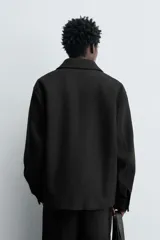 Chaquetón de corte regular fit en color negro, con cuello solapa, manga larga y cierre frontal con botones. Presenta dos bolsillos delanteros de plastrón con solapa en la cadera.