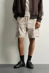 Bermuda cargo color negro de corte relaxed fit, confeccionada en tejido de algodón con elasticidad y efecto lavado. Cuenta con cintura elástica ajustable con cordón, bolsillos frontales y bolsillos laterales tipo cargo con solapa en las perneras.