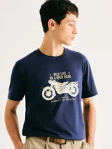Camiseta de corte regular color azul marino, con cuello redondo y mangas cortas. Presenta una estampa frontal en tonos claros que incluye la ilustración de una motocicleta y texto alusivo a la aventura.