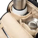 Bolso matero de diseño acolchado en color negro, con doble asa superior y correa ajustable extraíble. Presenta un compartimento principal con cierre doble, bolsillos externos con cierre y un parche circular con el logo de la marca en el frente.