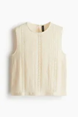 Blusa sin mangas color beige de tejido texturizado con efecto arrugado e inserciones verticales de encaje en el frente. Cuenta con escote redondo, abertura de cerradura con botón en la nuca y bajo recto.