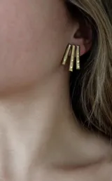 Aros dorados con forma de tres varillas verticales texturizadas.