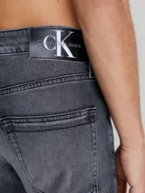 Pantalón de jean gris oscuro de corte slim, con cintura media, cinco bolsillos y cierre con cremallera.