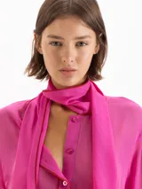 Camisa Brooklyn de gasa en color fucsia, confeccionada en seda y viscosa. Presenta mangas largas con puños abotonados, cierre frontal con botones y un elegante lazo integrado en el cuello.