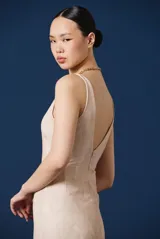 Vestido largo color beige, con escote en V, sin mangas y silueta ajustada que se ensancha levemente hacia el ruedo.