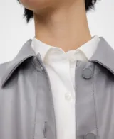 Chaqueta bomber gris con cuello italiano, cierre frontal con broches a presión y bajo abullonado. Las mangas son redondeadas con pinzas en los codos y cuenta con bolsillos verticales en las costuras laterales.