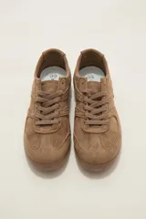 Zapatillas de estilo urbano color chocolate, confeccionadas en material textil tipo gamuza, con cordones al tono y suela de goma plana.