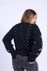 Sweater de punto negro con diseño de ochos, cuello redondo y detalles bordados a mano en color rosado en el frente y las mangas. Presenta un corte boxy con elástico ancho en la cintura y los puños.