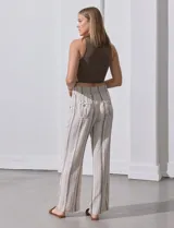 Pantalón largo de lino color beige con rayas verticales marrones. Tiene pretina ancha en punto smock con lazo ajustable, bolsillos verticales delanteros y bolsillos aplicados traseros.