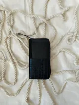 Billetera grande de cuero con cierre metálico perimetral. Presenta un diseño combinado con una sección superior de cuero liso brillante y una sección inferior de cuero con textura de reptil. Incluye el logo de la marca grabado en la parte frontal.