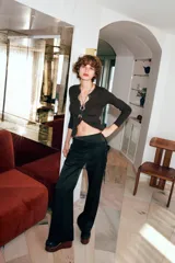 Pantalón largo de satén negro con pareo de encaje superpuesto en la cintura y lazada lateral. Cierre lateral con cremallera oculta.