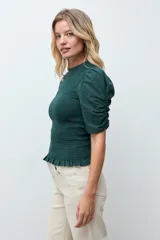 Blusa de color gris oscuro con diseño de punto smock en el cuerpo, cuello redondo y mangas cortas abullonadas con detalle de volados en el ruedo.