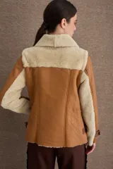 Chaqueta tipo gamulán de cuero color camel con interior y solapas de piel sintética en color beige. Presenta cierre frontal cruzado, correas ajustables con hebillas en los puños y en la cintura, y diseño de cuello solapa.