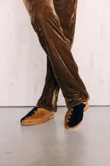Zapatos tipo mule de punta cerrada y talón abierto, con diseño bicolor en tonos dorado y mostaza, con detalles cruzados en el empeine y suela baja.