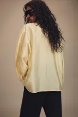Camisa de corte holgado confeccionada en tejido satinado con mezcla de lyocell. Presenta cuello redondo con escote en pico y lazada frontal integrada. Cuenta con mangas largas abullonadas terminadas en puños anchos y bajo recto.