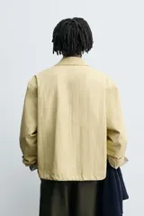 Cazadora de tejido con algodón, color amarillo pálido, con cuello solapa y cierre frontal de cremallera. Presenta bolsillos frontales de vivo y bajo ajustable con elástico en los laterales.