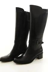 Bota de caña alta confeccionada en cuero legítimo color marrón, con diseño clásico, costuras visibles y una delicada tira con hebilla lateral. Cuenta con cierre lateral interno y taco medio ancho.