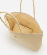 Cartera amplia confeccionada en fibra de papel, de color beige, con asas de hombro, cierre superior y detalle metálico dorado claro en el frente.