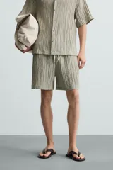 Bermuda negra de corte regular, confeccionada en tejido jacquard con efecto arrugado. Presenta cintura elástica ajustable con cordón blanco, bolsillos laterales y bolsillos traseros de vivo.