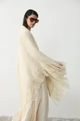 Ruana de punto color crudo, confeccionada en lana merino sin teñir con mezcla de lino y viscosa, con diseño triangular y terminación de flecos en los bordes.