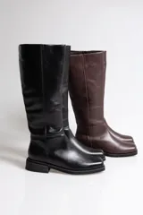 Botas de caña media confeccionadas en cuero vacuno, con diseño de punta redondeada y suela plana con pequeño taco cuadrado. Presentan costuras verticales decorativas a lo largo de la caña.