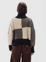 Polera de punto con diseño colorblock en tonos neutros, cuello alto, hombros caídos y mangas largas. Presenta puños, cuello y ruedo acanalados en color negro.